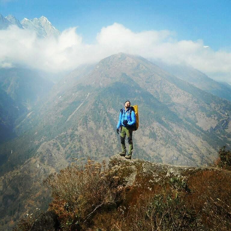 Bhuwan on a ridge outcrop above a cloud-filled valley, pack on